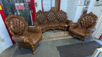 Antique-style brown leather 2-seater and armchair with carved wooden arms and backs, perfect for classic home décor.