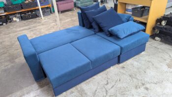 Corner sofa in blue fabric with matching cushions, versatile and stylish for contemporary living rooms. Perfect for relaxing and entertaining, this refurbished sofa offers comfort and durability.
