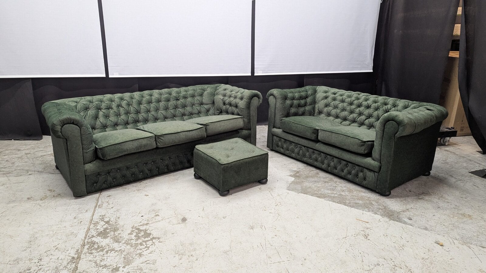 Elegant green Chesterfield sofas with matching footstool Two green Chesterfield sofas with button-tufted upholstery and rolled arms, complemented by a small matching footstool, ideal for classic living room decor.