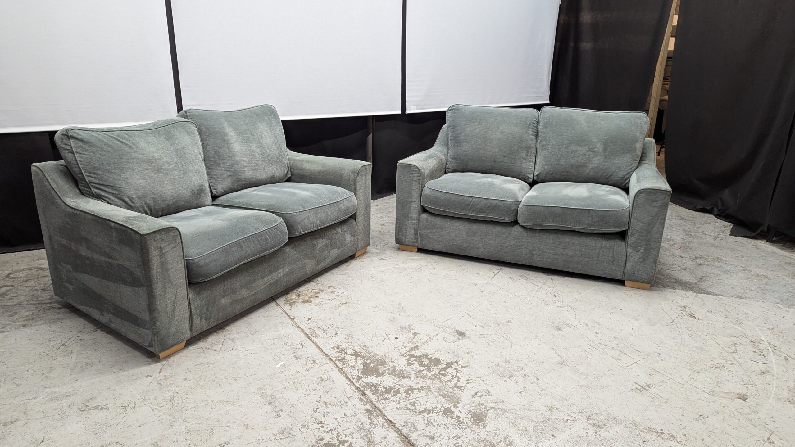 Modern grey fabric 2-seater sofas in showroom Two grey fabric 2-seater sofas with plush cushions and wide armrests.